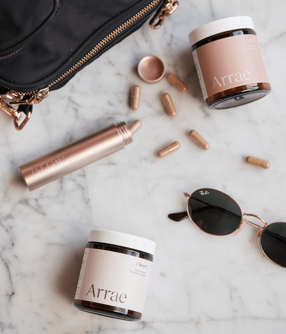 Arrae Bloat Capsules, Calm Capsules, & Carry-on Capsule Case laying next to purse and sunglasses