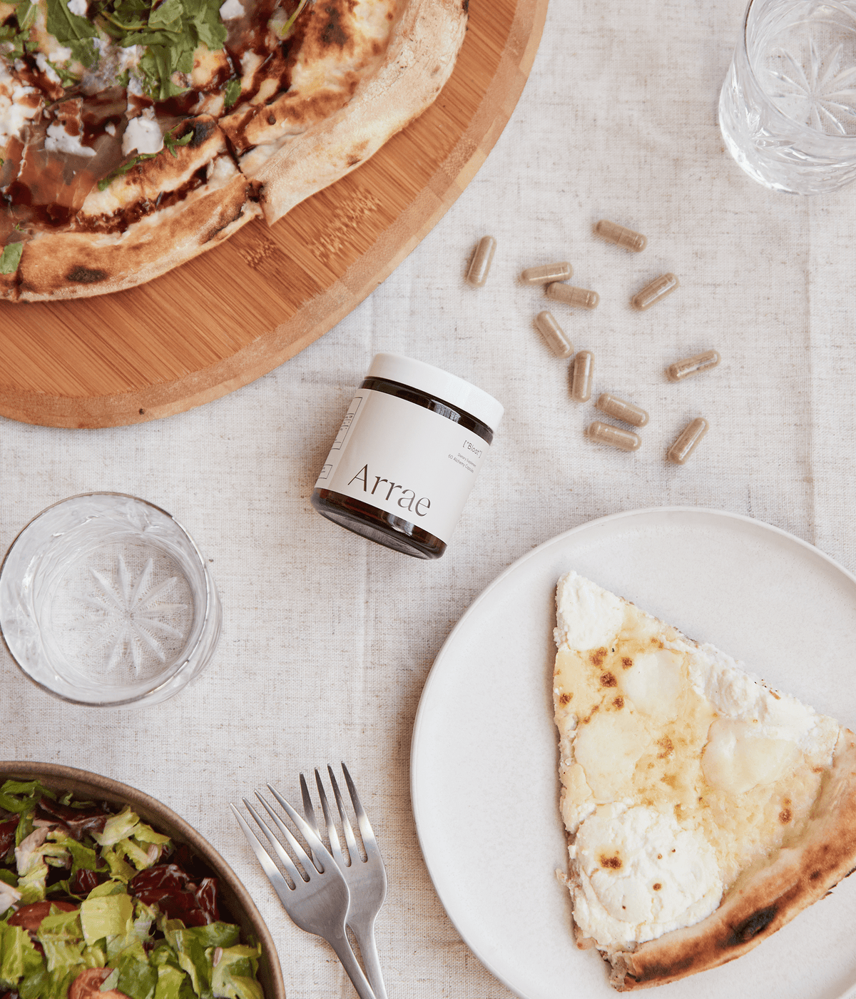 Arrae Bloat Capsules laying on the table next to pizza & salad
