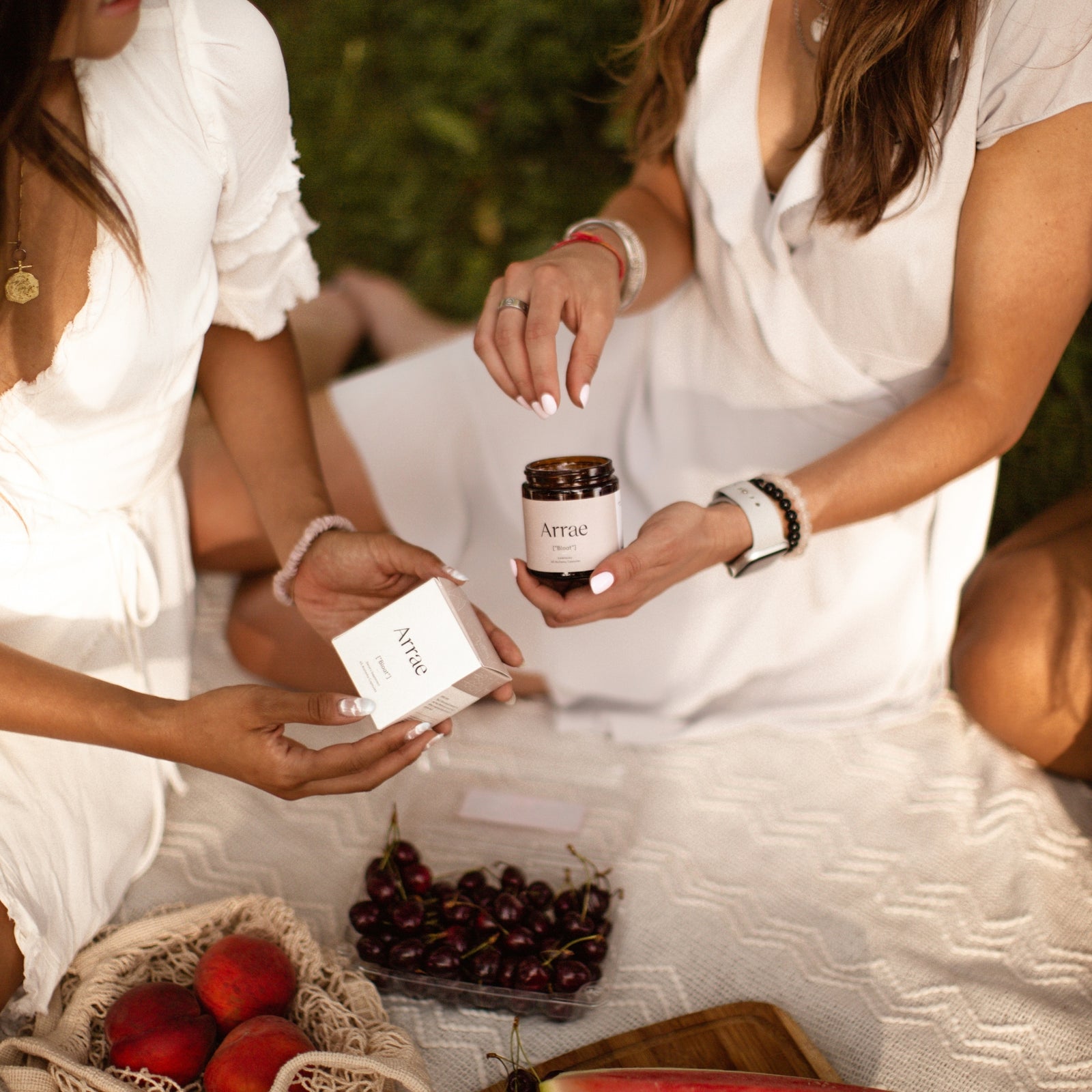 Two women sitting on a planet with fresh fruit, looking at Arrae products.