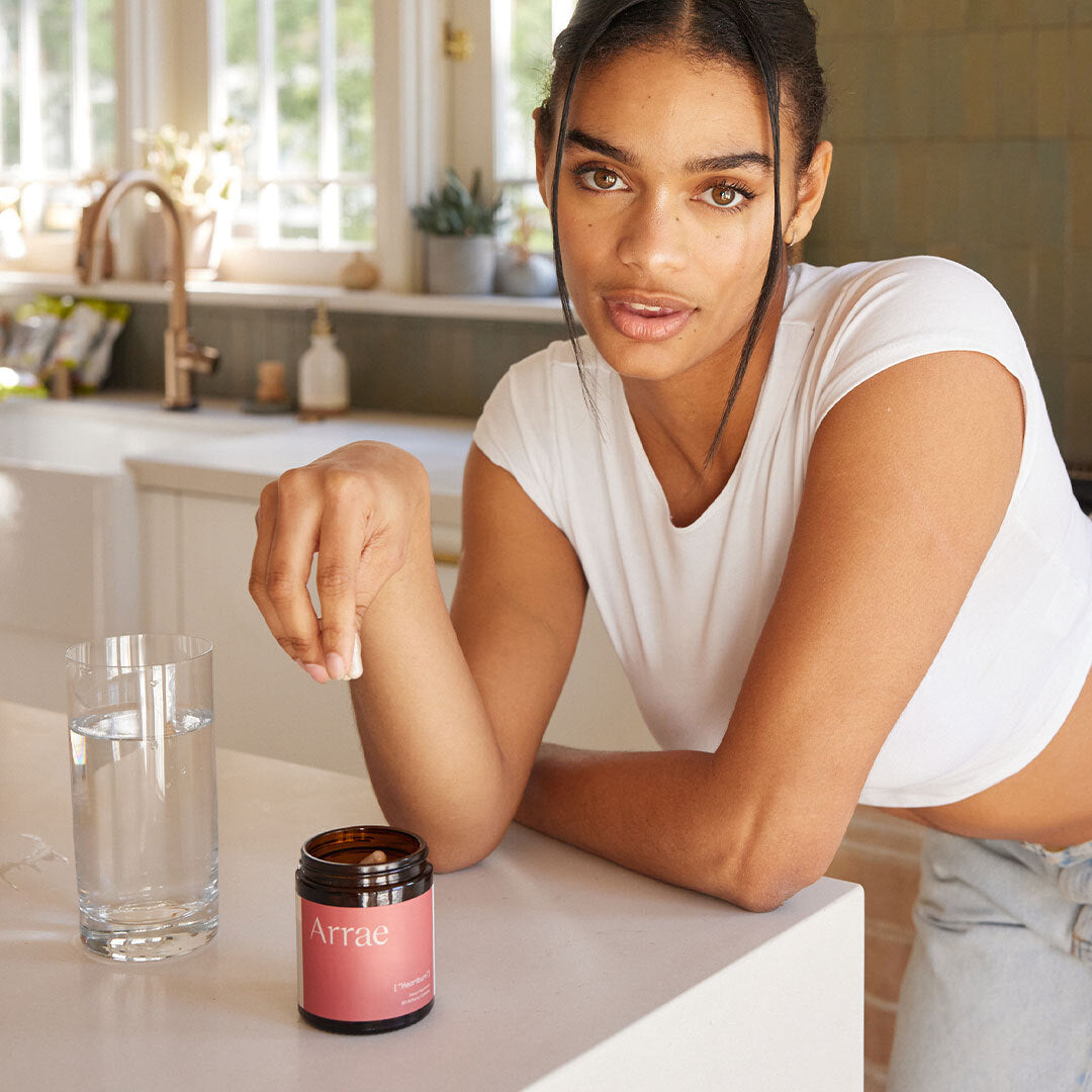 A woman holding an Arrae Heartburn capsule in her hand, with the jar on the counter, showcasing the product