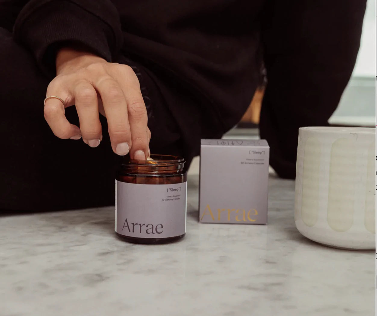 Hand going into a jar of Arrae Sleep Supplement - A bottle of 60 capsules featuring a blend of natural ingredients, designed to promote restful sleep and relaxation without melatonin.