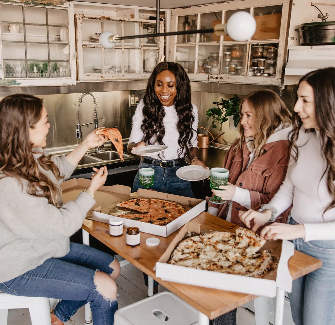 Lifestyle image of 4 woman, 2 pizzas, and Arrae products showcased on the table