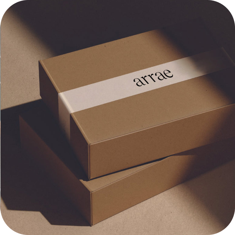 Two kraft paper boxes with a white band that has the brand name Arrae printed on it. The boxes are arranged on a surface with soft lighting casting shadows, giving a minimalist and elegant look.
