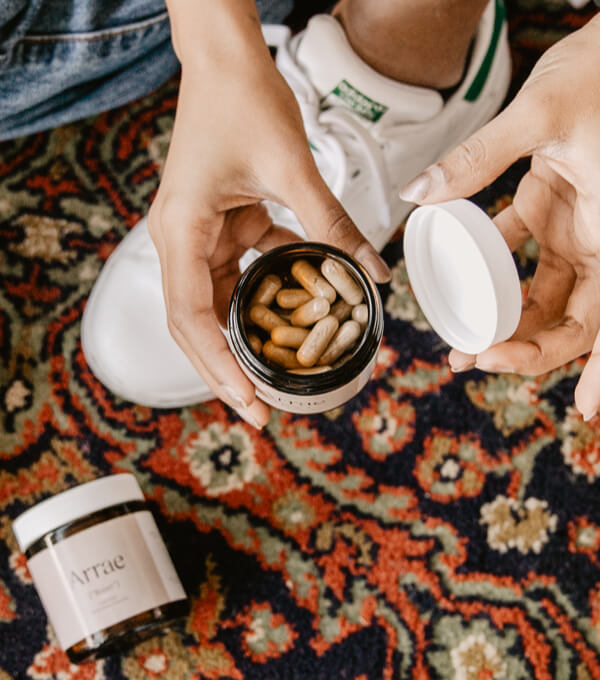 A top view of an open bottle of bloat pills over a decorative persian rug. The capsules are about 1/4 the size of the persons thumb holding the bottle